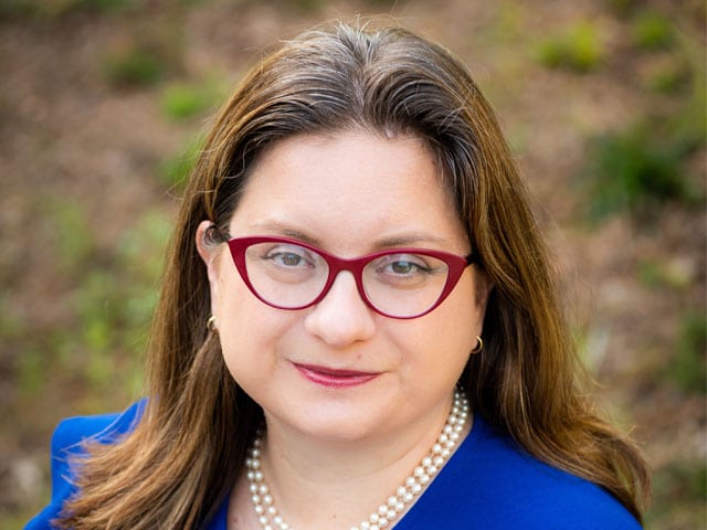 A photo of Larysa Kautz, the President and CEO of Melwood Inc, wearing glasses, a necklace, and a blue top.