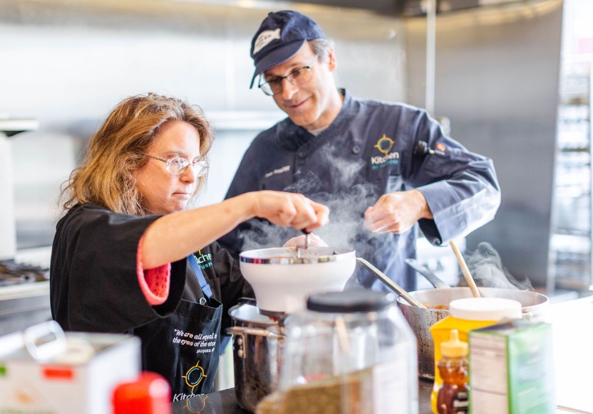 A photo of the program leader, Dan Traster, guiding a student as she prepares food in a professional kitchen setting.