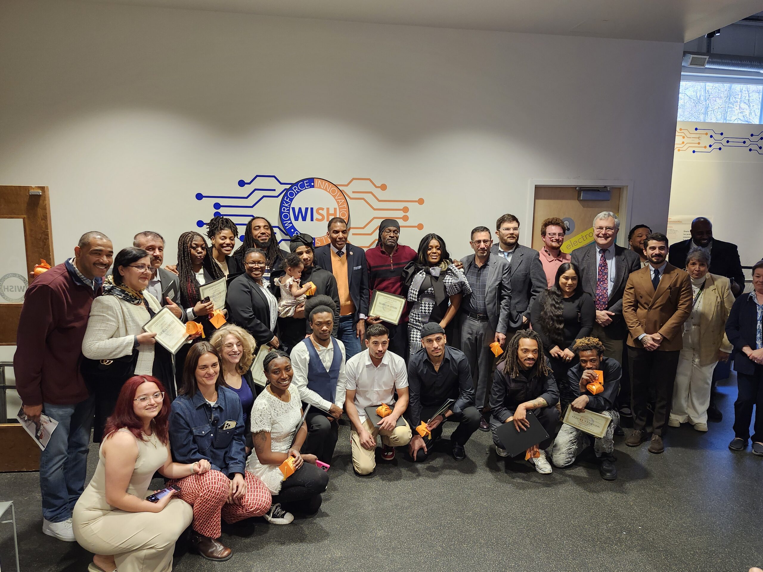 large group of Building Paths graduates and staff before a WISH Center sign