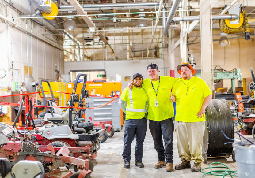 Three men in yellow shirts standing together in a warehouse at Fort Meade
