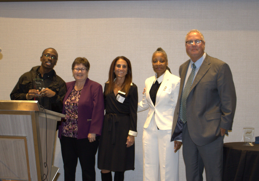 Montrell smiling and posing with his award on stage with four other people