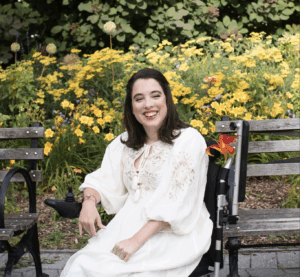 Anastasia Somoza, smiling and wearing white sitting outdoors in front of yellow flowers