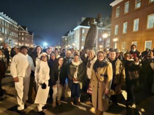 A group of people posing for a group shot among a crowd at night and in front of a statue