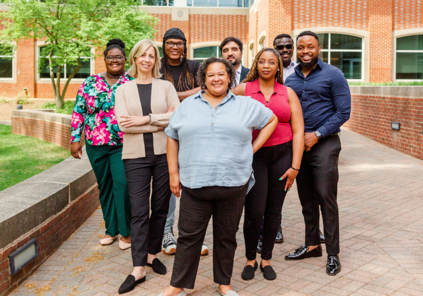 A group of eight individuals in business casual attire in a courtyard, smiling at the camera