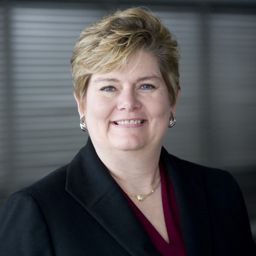 Photo of a woman with short hair in a business suit in front of a window.