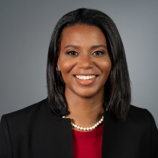 Headshot of a woman with a red shirt under a black suit jacket.