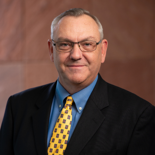 Headshot of a man with glasses and a yellow tie in a black suit,