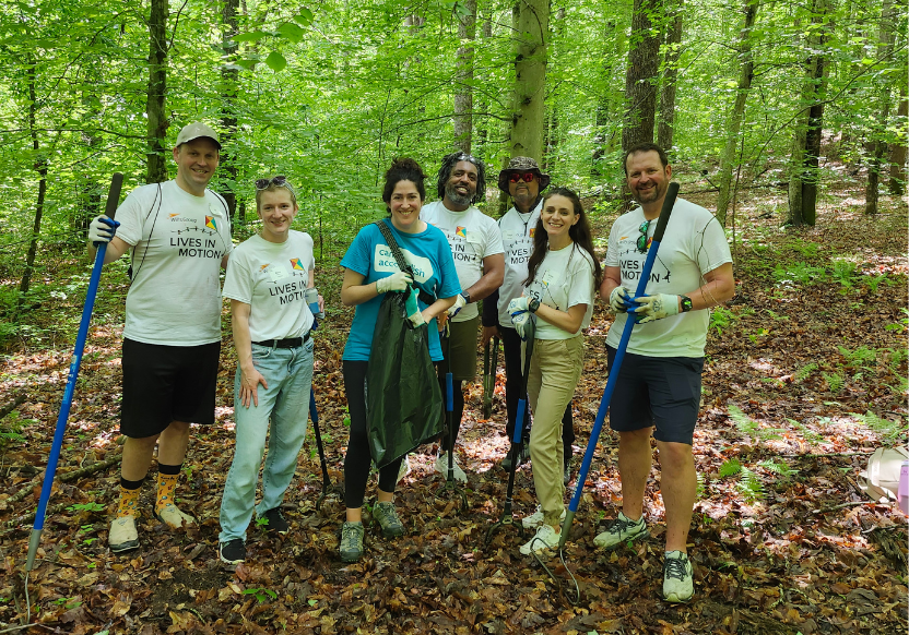 a group of seven people in the woods, all smiling. Most are wearing matching Wills Group T-shirts