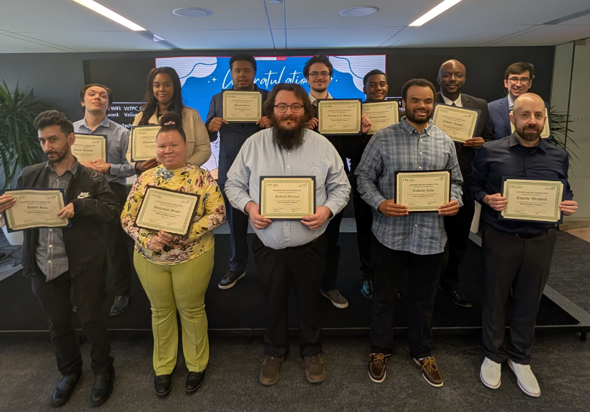 A group of 12 people, smiling and in business casual attire, hold certificate in front of them
